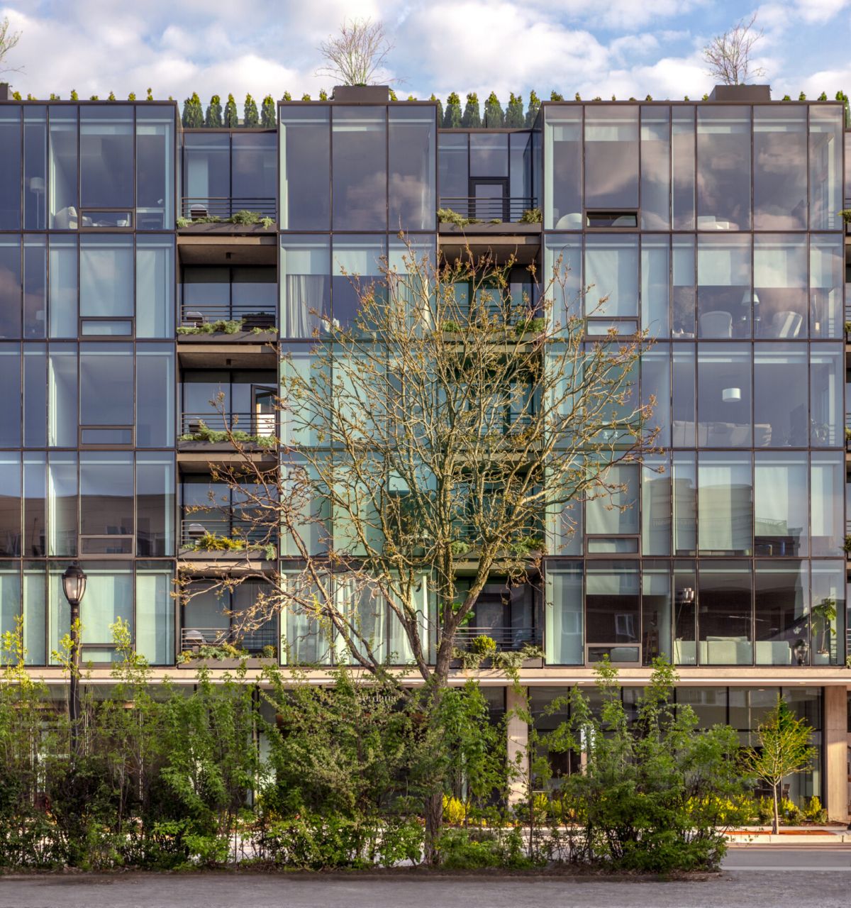 Optima Verdana luxury apartment with Modern glass apartment building, Optima Verdana, with balconies and greenery on the North Shore; a person walks by on a sunny day.