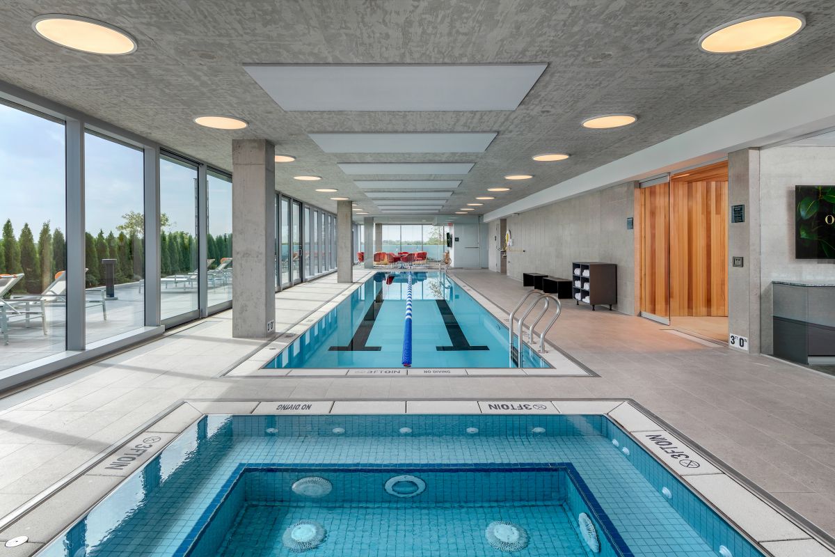 Optima Verdana luxury apartment with Modern indoor pool area with lap pool, hot tub, Recovery Circuit, lounge chairs, large windows, and a sauna room.