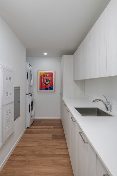 Optima Verdana luxury apartment with Modern laundry room with stacked washer and dryer, white cabinets, and colorful abstract art on the wall.
