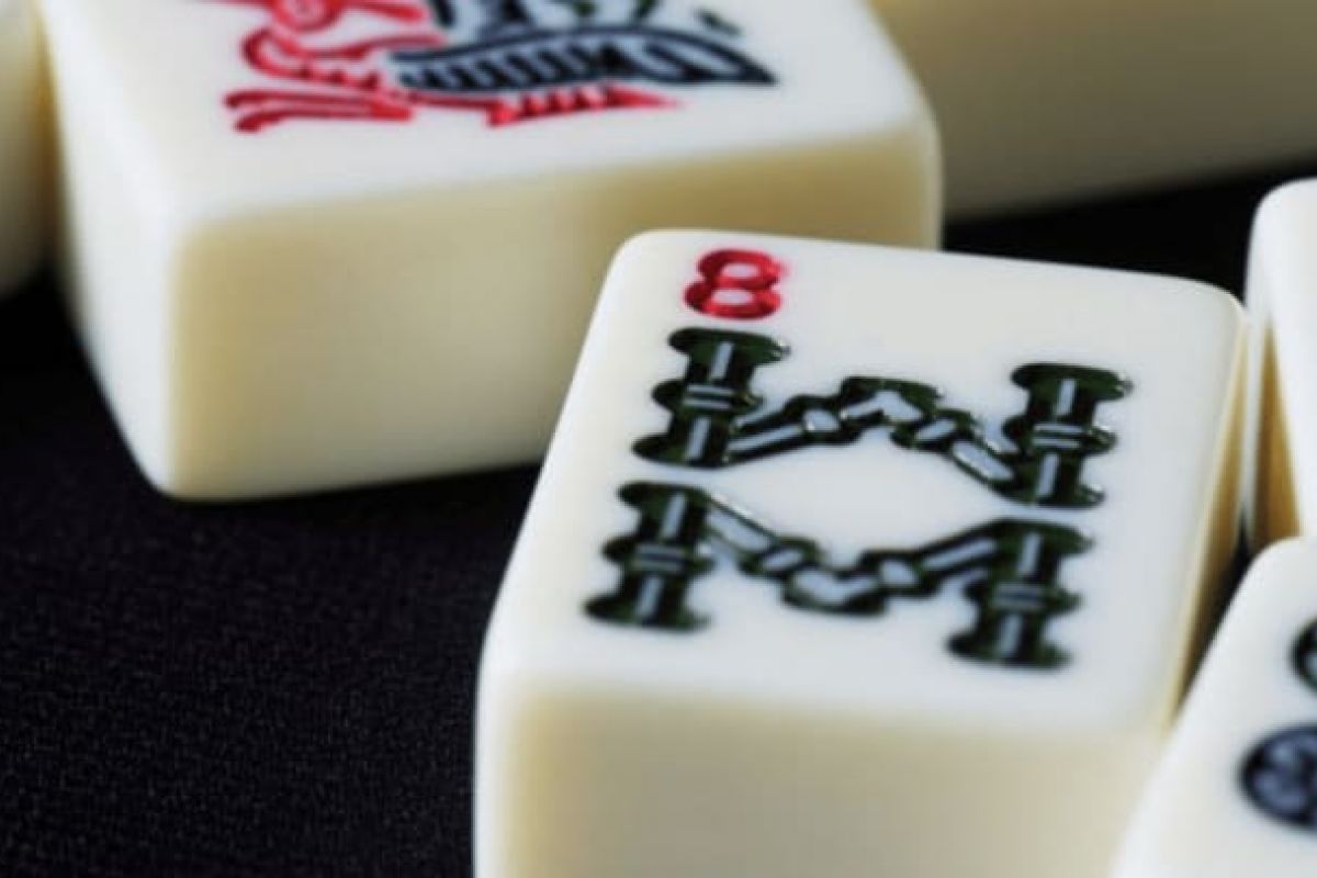 Optima Verdana luxury apartment with Close-up of Mahjong tiles, with an 8 of bamboo tile in focus, echoing the rich origins of Mahjong on a dark surface.