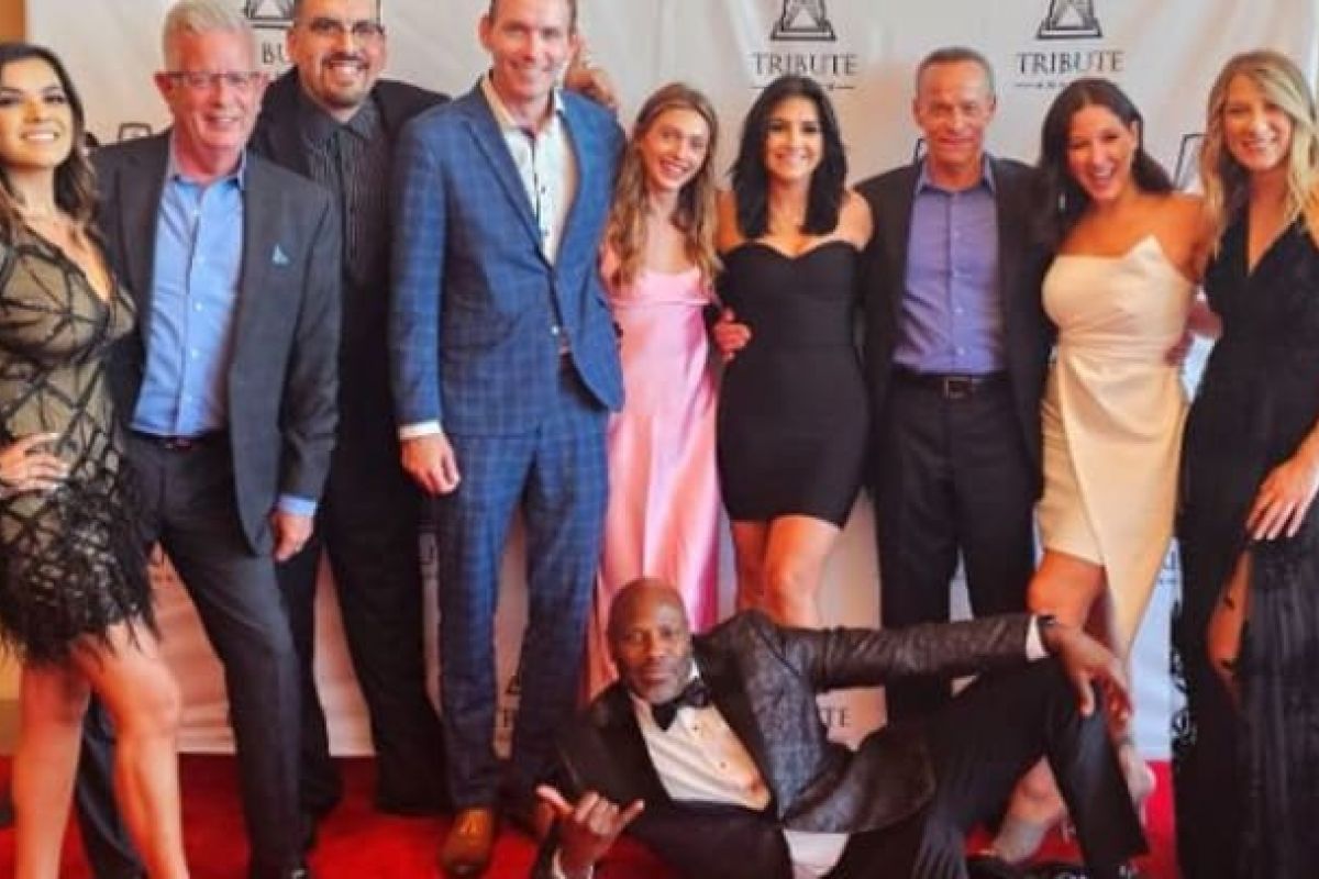 Optima Verdana luxury apartment with The Optima Team poses formally, smiling on the red carpet at the 2023 AMA Tribute Awards before a Tribute-branded backdrop.