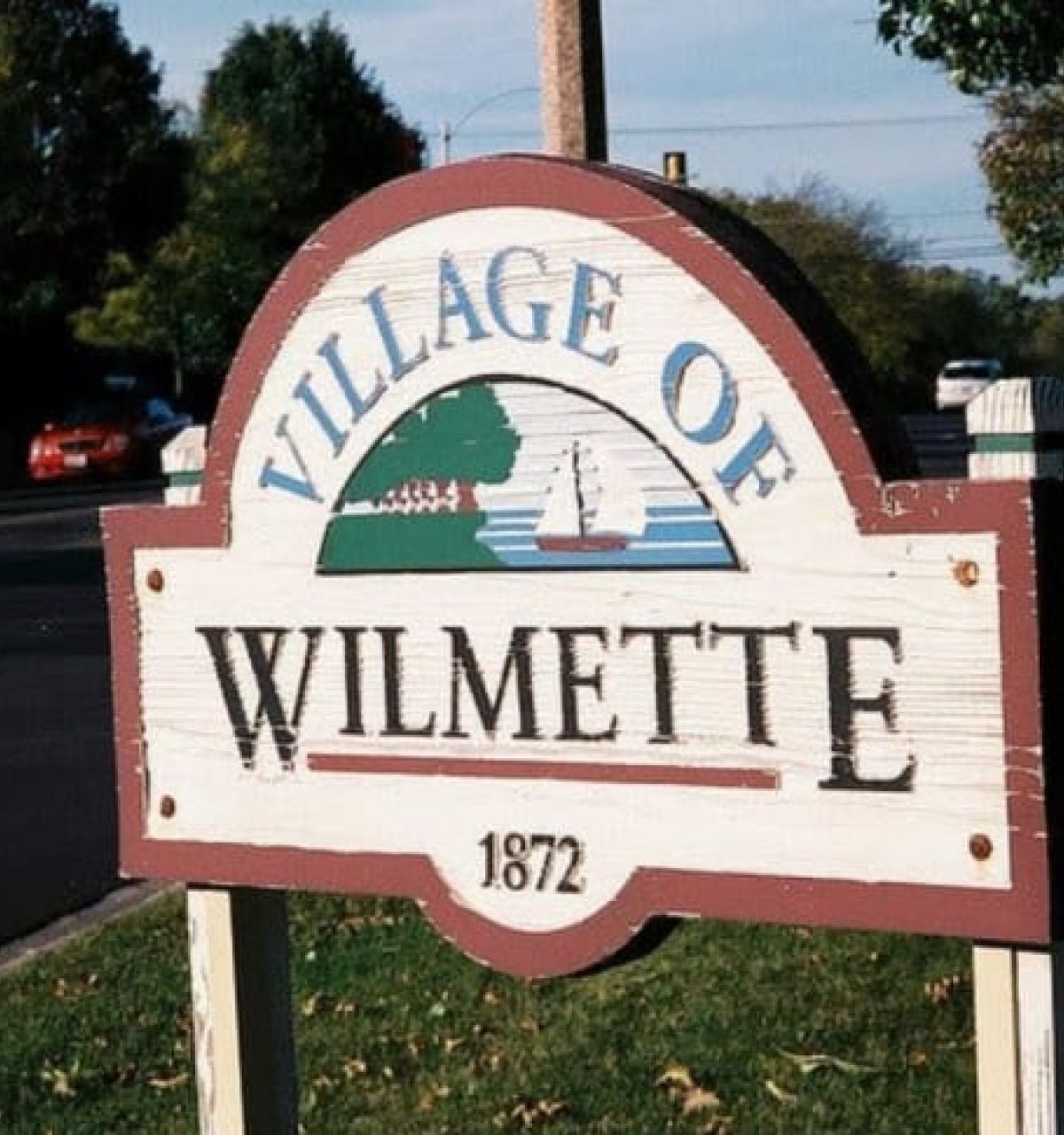 Optima Verdana luxury apartment with Wooden sign reading "Village of Wilmette 1872" with a sailboat, trees, street, and captured for the Wilmette Sesquicentennial Photography Project.