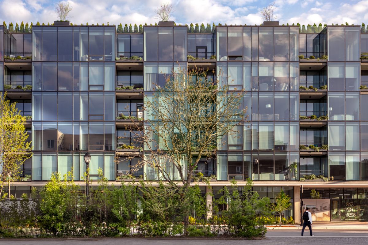 Optima Verdana luxury apartment with Modern glass apartment building, Optima Verdana, with balconies and greenery on the North Shore; a person walks by on a sunny day.