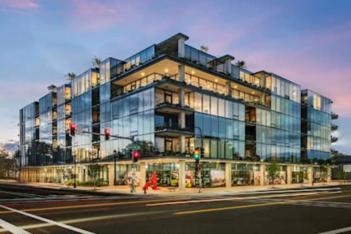 Optima Verdana luxury apartment with Modern glass building at a street corner, Optima Verdana features shops below, balconies above, and sunset greenspace views.