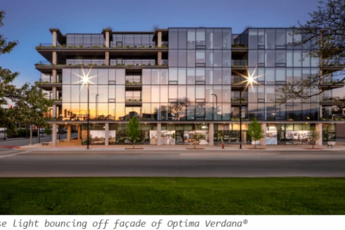 Optima Verdana luxury apartment with A modern glass building reflecting sunrise light, showcasing daylight design and modern architecture, with trees and a quiet street in front.