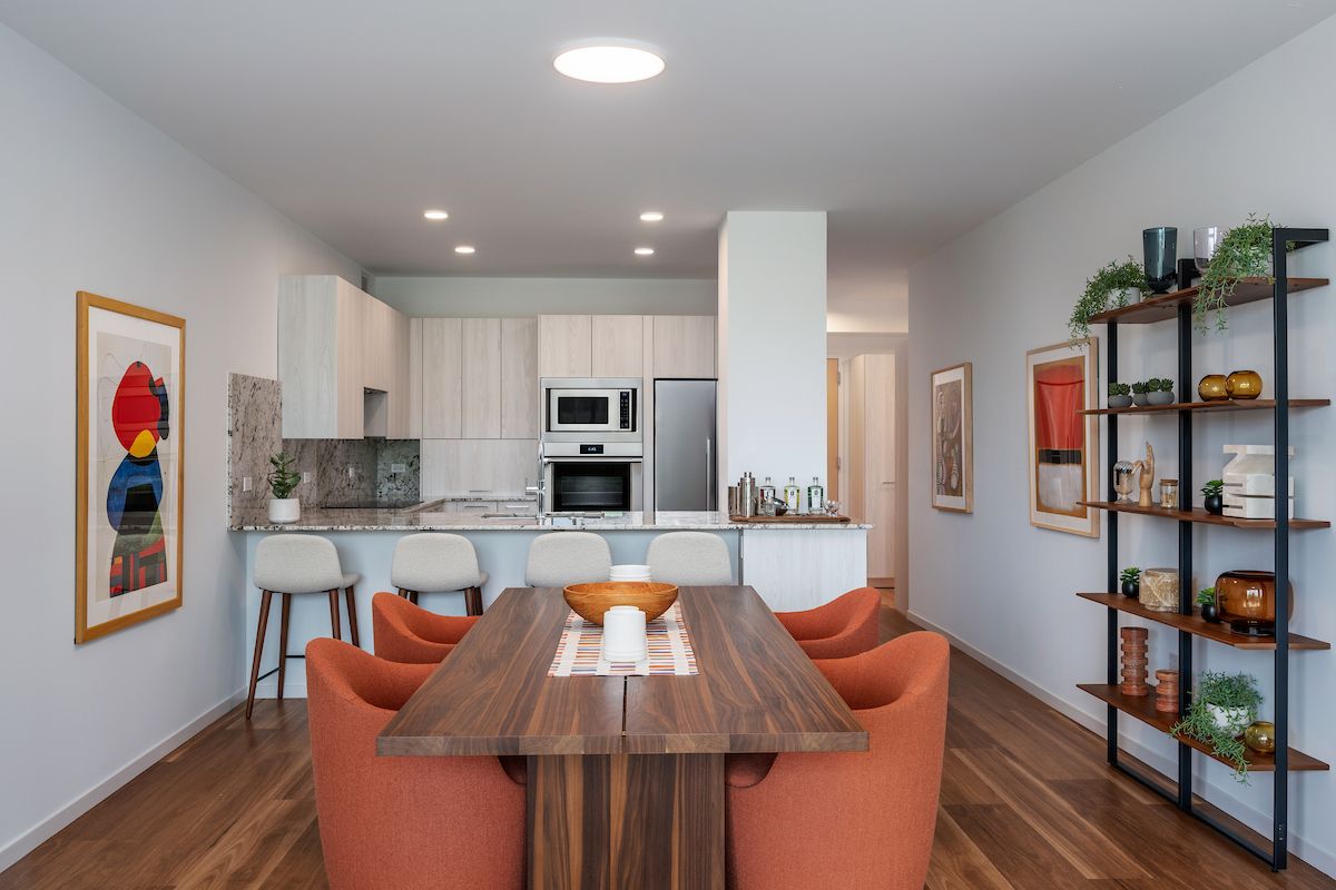 Optima Verdana luxury apartment with Modern dining area with wooden table, orange chairs, open kitchen, and minimalist decor with plants and art.
