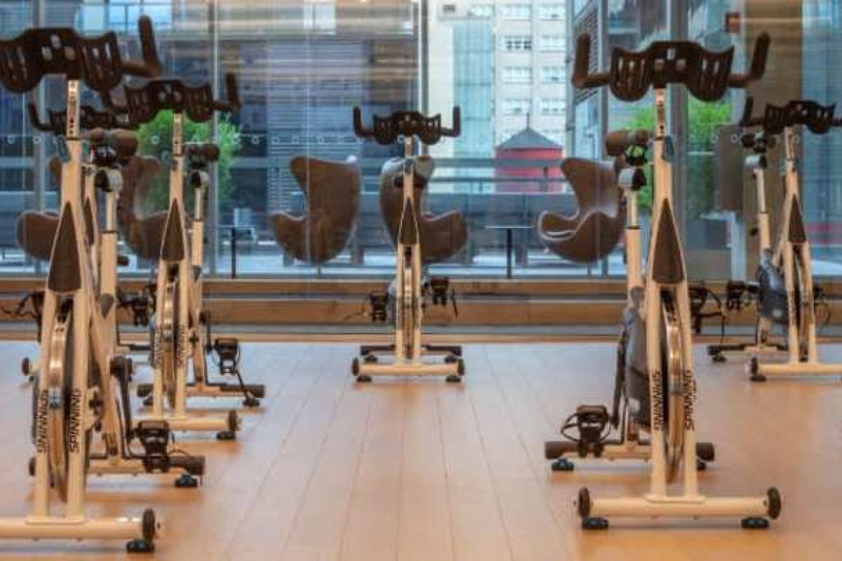 Optima Verdana luxury apartment with Stationary bikes arranged in rows for indoor cycling in a bright gym with large windows and city views.