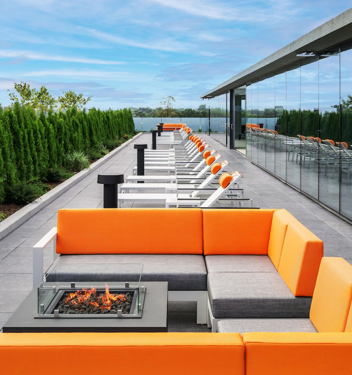 Optima Verdana luxury apartment with Modern rooftop patio with orange seating, a fire pit, lounge chairs, and green trees along the edge.