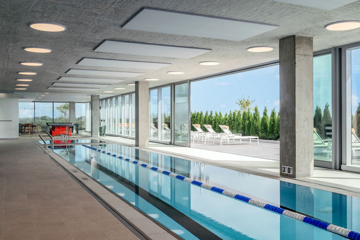 Optima Verdana luxury apartment with Indoor lap pool with blue lane dividers, floor-to-ceiling windows, and lounge chairs outside on a sunny day.