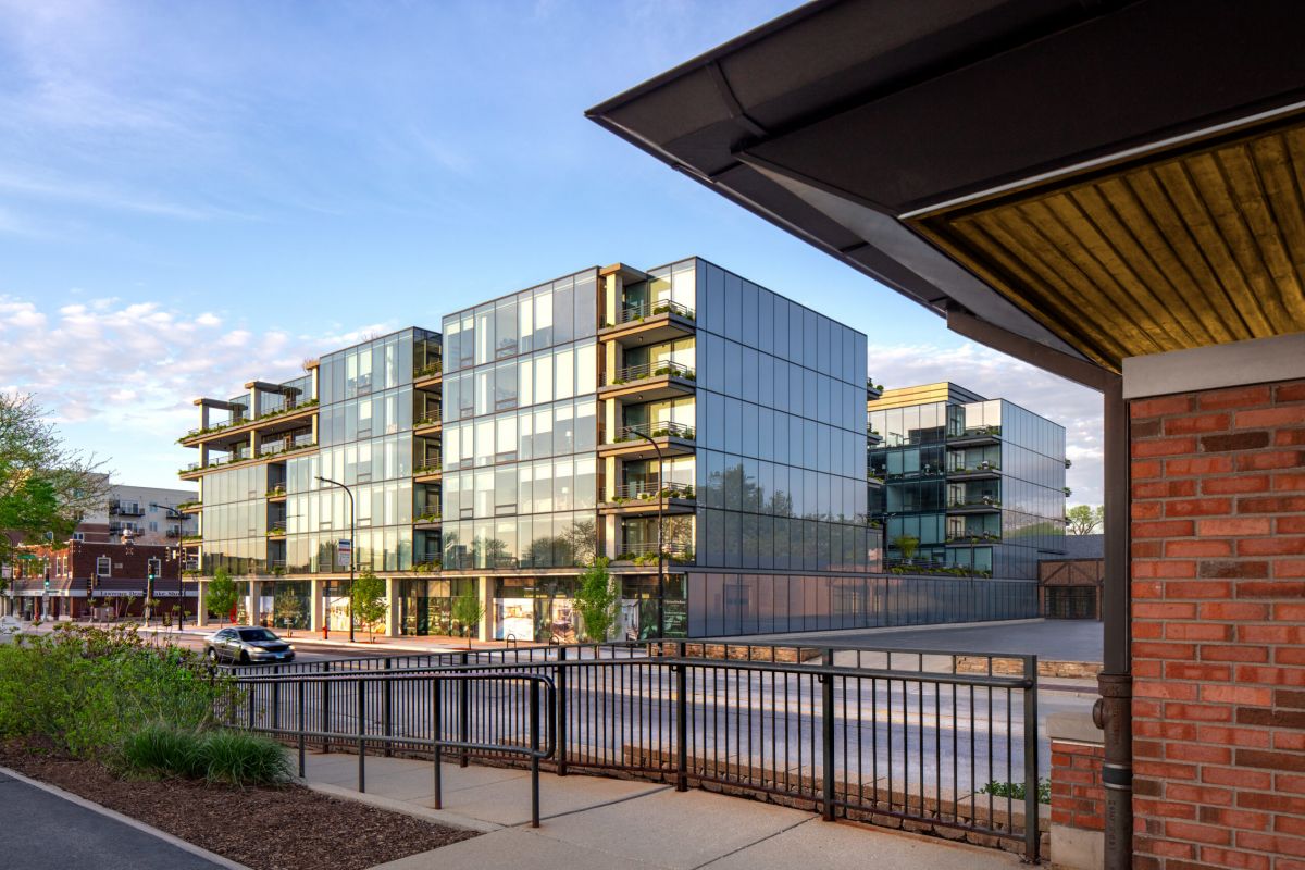 Optima Verdana luxury apartment with Modern glass apartment with balconies beside a street offers short commute benefits, viewed from across a fence and sidewalk.