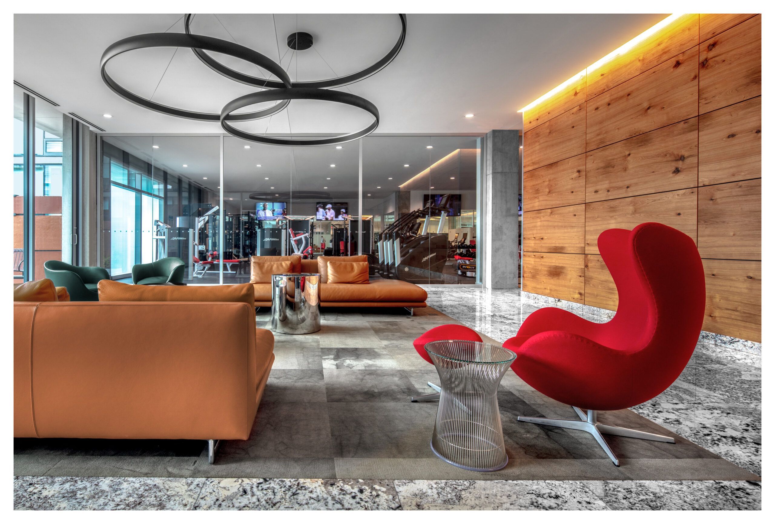 Optima Verdana luxury apartment with Modern lounge area at Optima Verdana with leather sofas, a red chair, and a glass wall showing the gym—built to last for years.