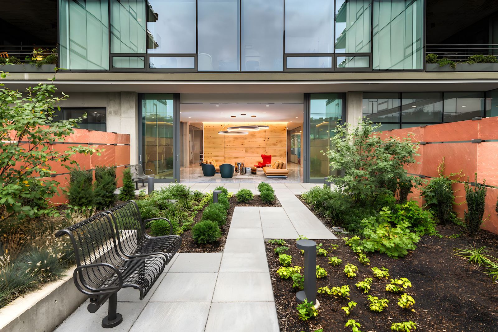Optima Verdana luxury apartment with Modern garden patio with a black bench, greenery, and glass doors leading to a brightly lit lounge area.