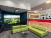 Optima Verdana luxury apartment with Green sofas and a glass table face a golf simulator screen; a basketball court is visible in the background.