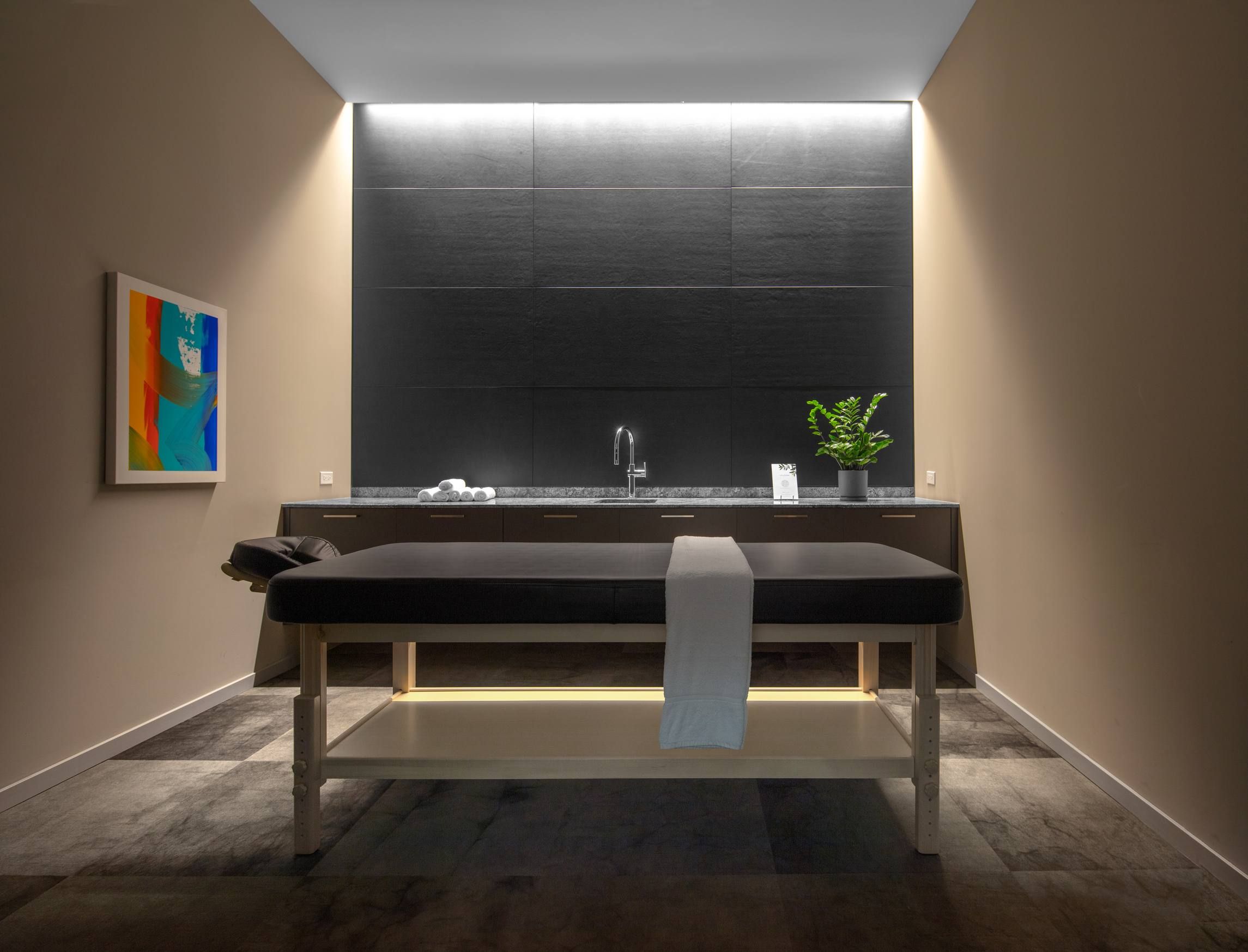Optima Verdana luxury apartment with Modern spa room with a massage table, wall art, sink, and a plant on a dark counter.