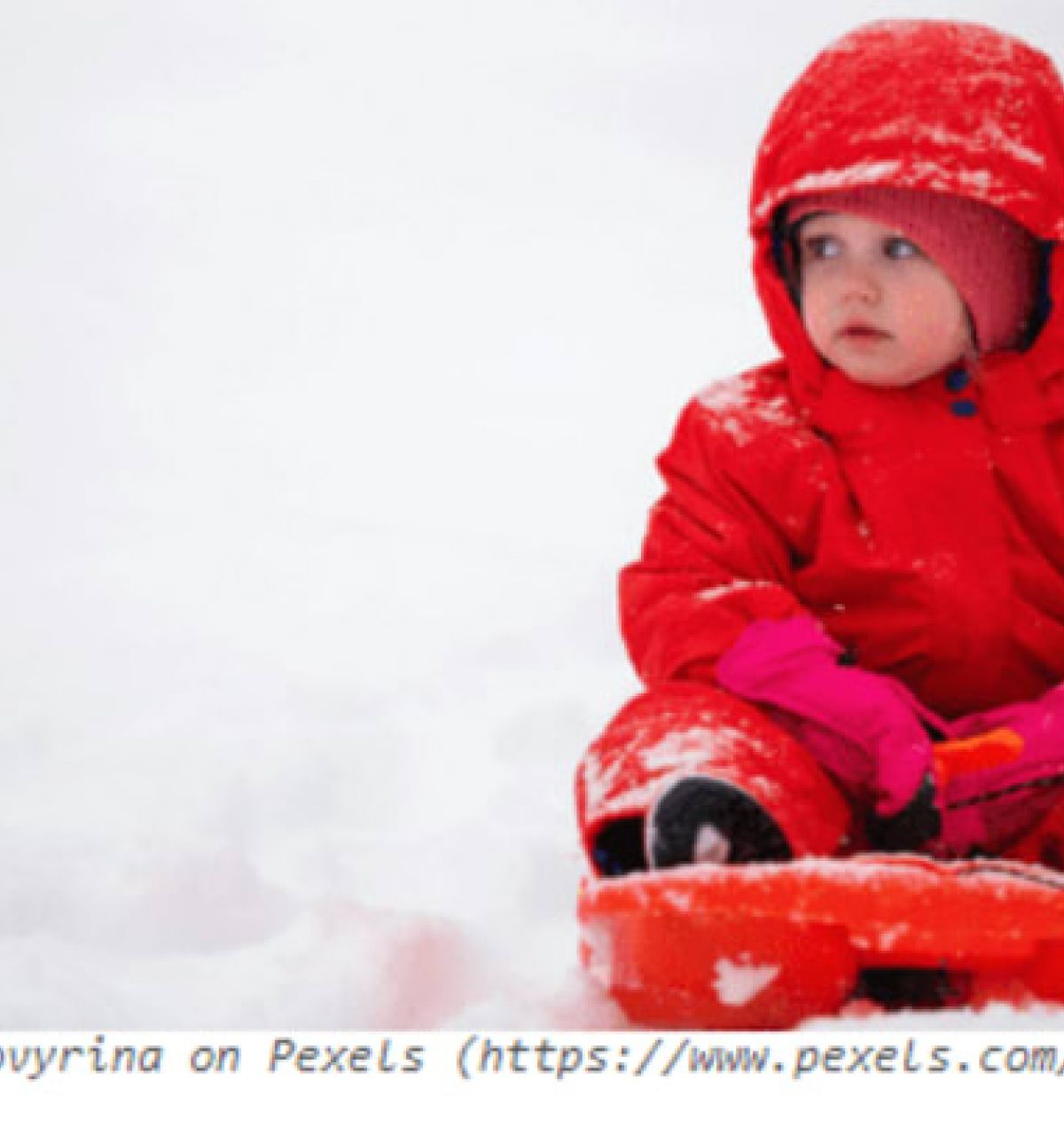 Optima Verdana luxury apartment with A young child in a red snowsuit sits on a sled, ready for winter fun on the snowy sledding hills.