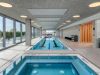 Optima Verdana luxury apartment with Modern indoor pool area with lap pool, hot tub, Recovery Circuit, lounge chairs, large windows, and a sauna room.