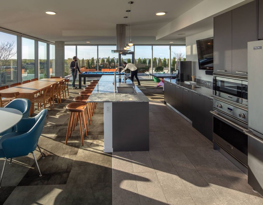 Optima Verdana luxury apartment with Modern communal kitchen and dining area with large windows, two people playing pool in the background.