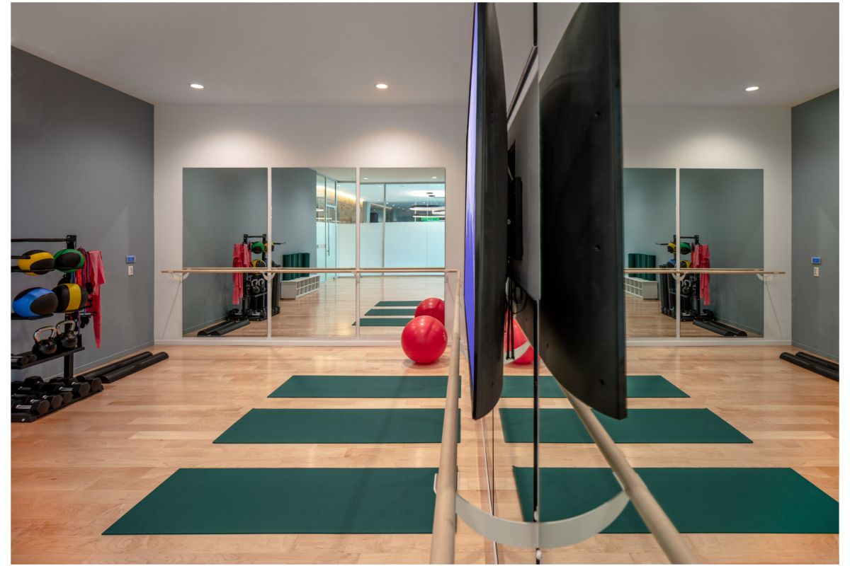 Optima Verdana luxury apartment with Exercise studio at Optima Verdana with yoga mats, Pilates balls, weights, mirrors, TV, wood floors, and modern lighting.