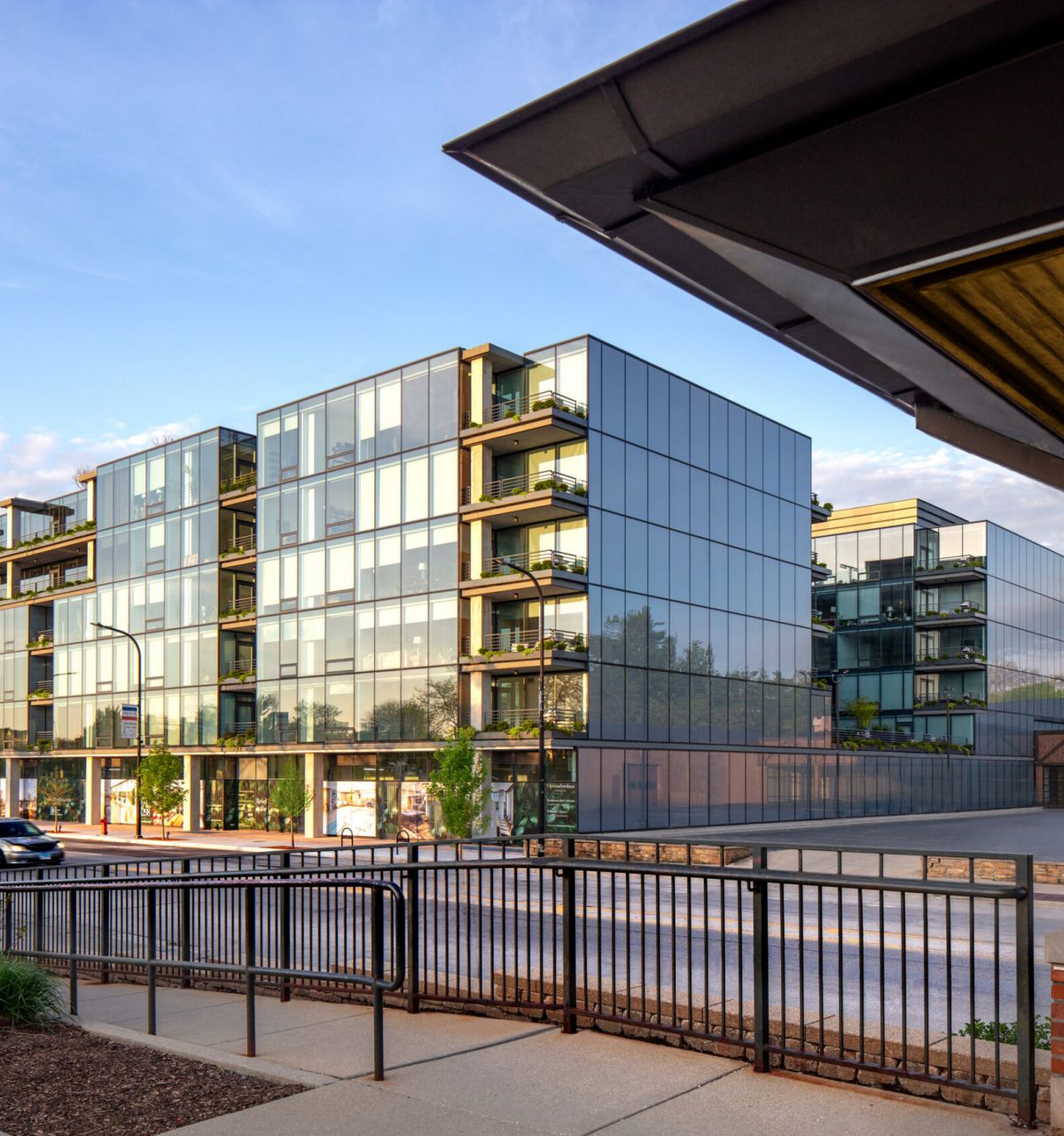 Optima Verdana luxury apartment with Modern glass apartment with balconies beside a street offers short commute benefits, viewed from across a fence and sidewalk.