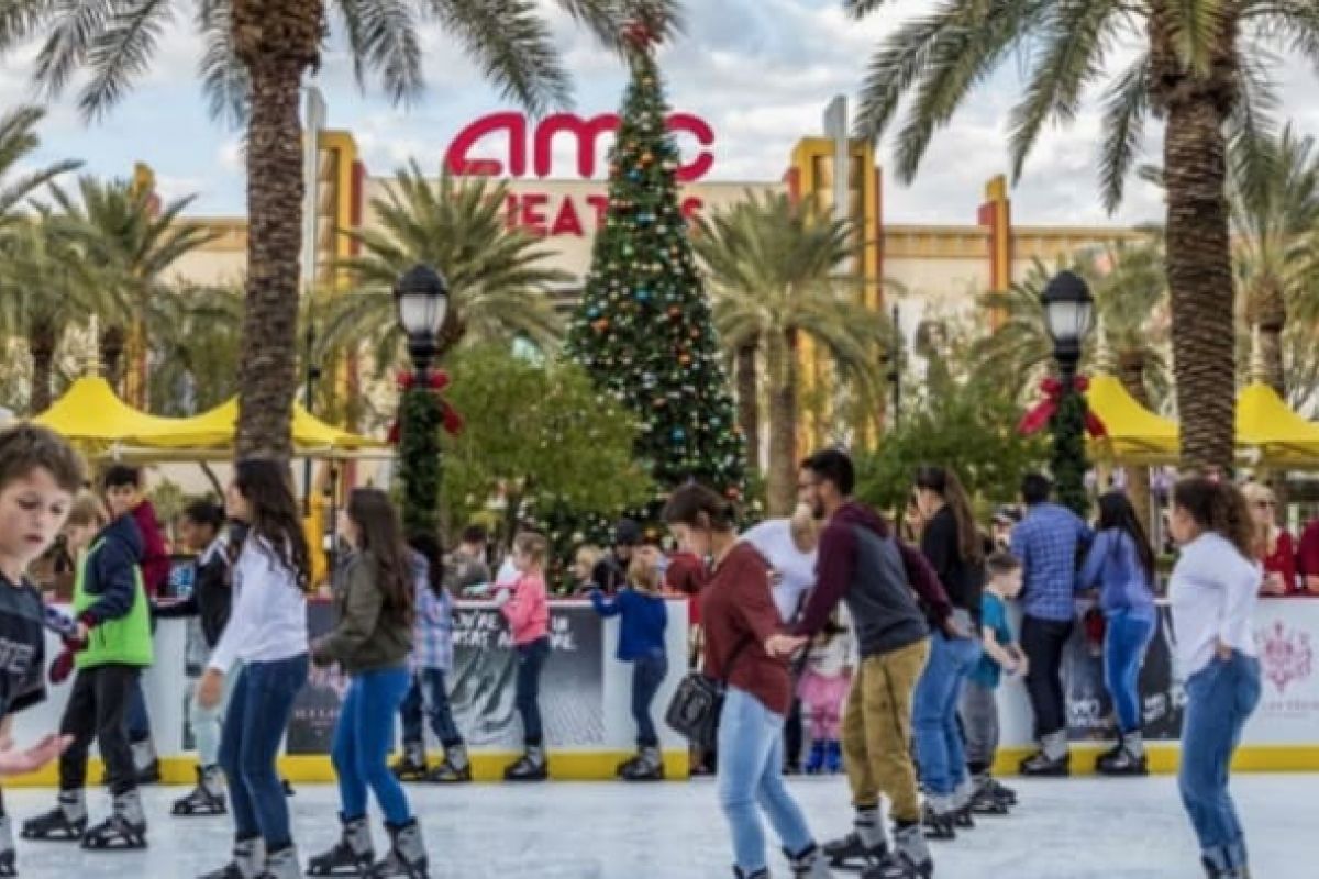 Optima Verdana luxury apartment with People ice skating outdoors by a Christmas tree and palm trees at Optima, with AMC Theatres in the background. Thanksgiving 2023 vibes.