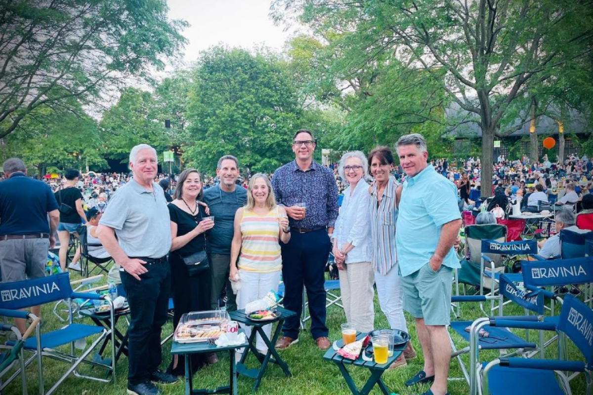 Optima Verdana luxury apartment with Eight adults smile at an outdoor Optima Connect gathering, enjoying the perks of community, with chairs, trees, and a crowd in the background.