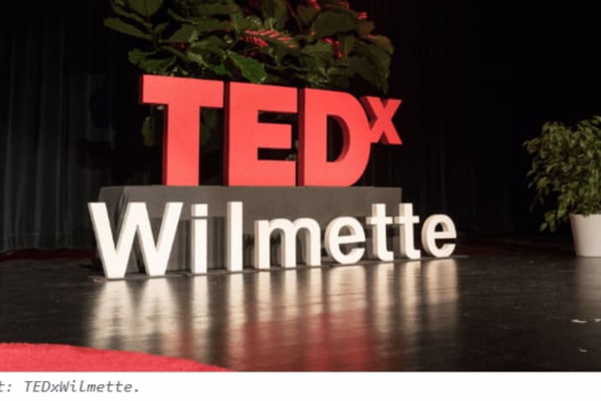 Optima Verdana luxury apartment with Large "TEDx Wilmette" sign on stage with plants in the background, featuring co-organizer Ami Campbell of TEDxWilmette.