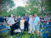 Optima Verdana luxury apartment with Eight adults smile at an outdoor Optima Connect gathering, enjoying the perks of community, with chairs, trees, and a crowd in the background.