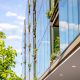 Optima Verdana luxury apartment with Modern glass building with plants growing on balconies, reflecting blue sky and surrounding greenery.