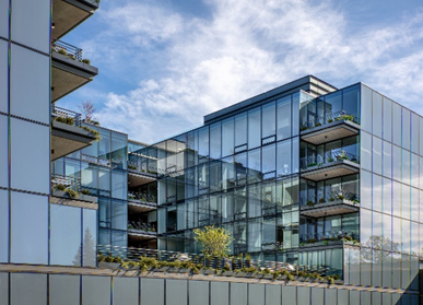 Optima Verdana luxury apartment with Modern glass apartment building with balconies and greenery under a partly cloudy sky.