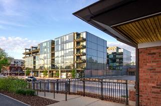 Optima Verdana luxury apartment with Modern glass apartment building with balconies, reflecting the sky, next to a brick structure and a fenced sidewalk.