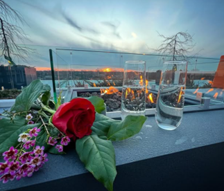 Optima Verdana luxury apartment with A red rose, small flowers, and two glasses sit on a ledge with a sunset and fire pit in the background.