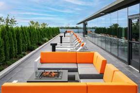 Optima Verdana luxury apartment with Modern rooftop patio with orange seating, fire pits, lounge chairs, and glass wall reflecting the sky.