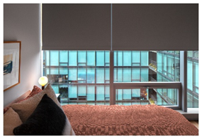 Optima Verdana luxury apartment with A modern bedroom with brown bedding and large windows overlooking a glass building.