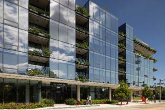Optima Verdana luxury apartment with Modern glass building with balconies and greenery, reflecting blue sky and clouds, street view.