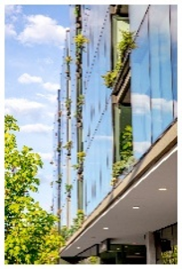 Optima Verdana luxury apartment with Modern glass building with small plants growing on its facade, set against a blue sky with clouds.