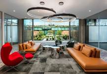 Optima Verdana luxury apartment with Modern lounge with orange sofas, red chair, and large windows overlooking a courtyard.