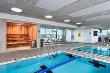 Optima Verdana luxury apartment with Indoor pool area with a lap pool, hot tub, and a glass-walled sauna; modern decor and large windows.