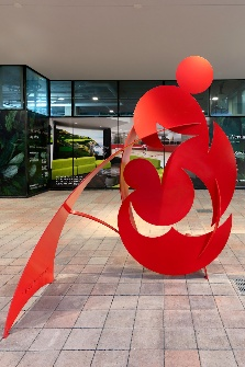 Optima Verdana luxury apartment with Bright red abstract metal sculpture on tiled floor, beside Optima Verdana’s green posters and glass walls—reflecting years of experience.