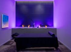 Optima Verdana luxury apartment with A modern spa room with purple lighting, a massage table, candles on a counter, and abstract art on the wall.