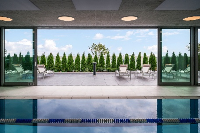 Optima Verdana luxury apartment with Indoor pool with view of lounge chairs and trees on an Optima outdoor space patio under a partly cloudy sky.
