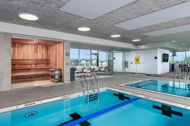Optima Verdana luxury apartment with Indoor pool area with a lap pool, hot tub, glass-walled sauna, and seating area in a modern building.