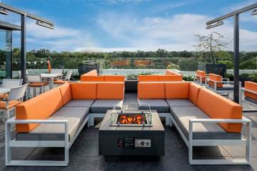 Optima Verdana luxury apartment with Modern outdoor patio with orange and gray sofas around a fire pit, overlooking trees under a blue sky.