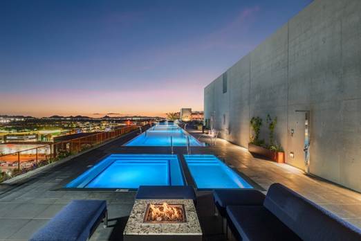 Optima Verdana luxury apartment with Rooftop pool and hot tub at sunset, with city views, lounge seating, and a fire pit in the foreground.