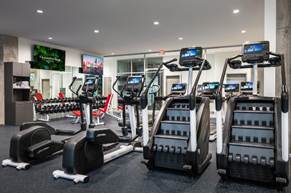 Optima Verdana luxury apartment with Modern gym with treadmills, stair climbers, weight racks, and TV screens, featuring clean, bright, and spacious workout space.