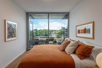 Optima Verdana luxury apartment with A modern bedroom with an orange bedspread, large windows, balcony, and framed art on white walls.