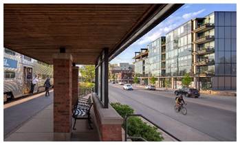 Optima Verdana luxury apartment with A commuter train platform overlooking a city street with a cyclist and Optima Verdana modern buildings, embodying the small rituals of daily wellness.
